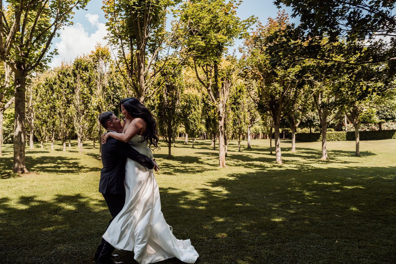 Groom dips bride for a romantic kiss in a sunlit garden setting.