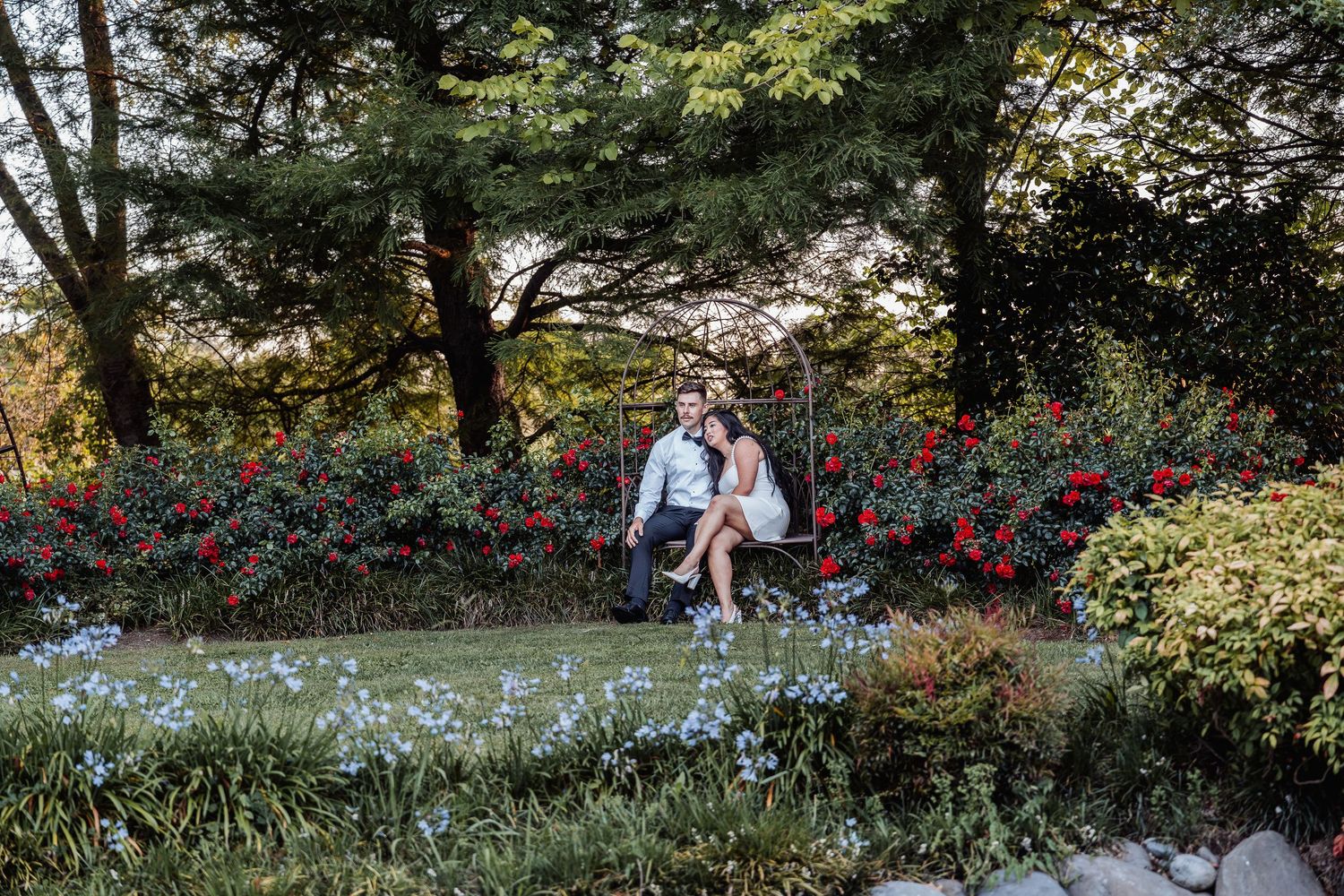 Couple sharing a romantic moment seated together among vibrant red and blue flowers in a garden.