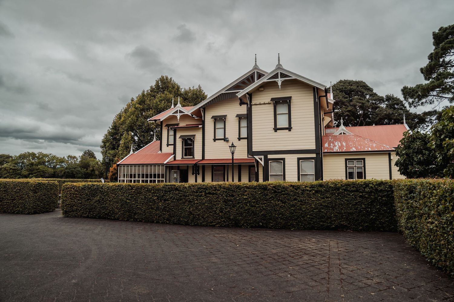 Historic Victorian manor house with manicured hedges under overcast skies.