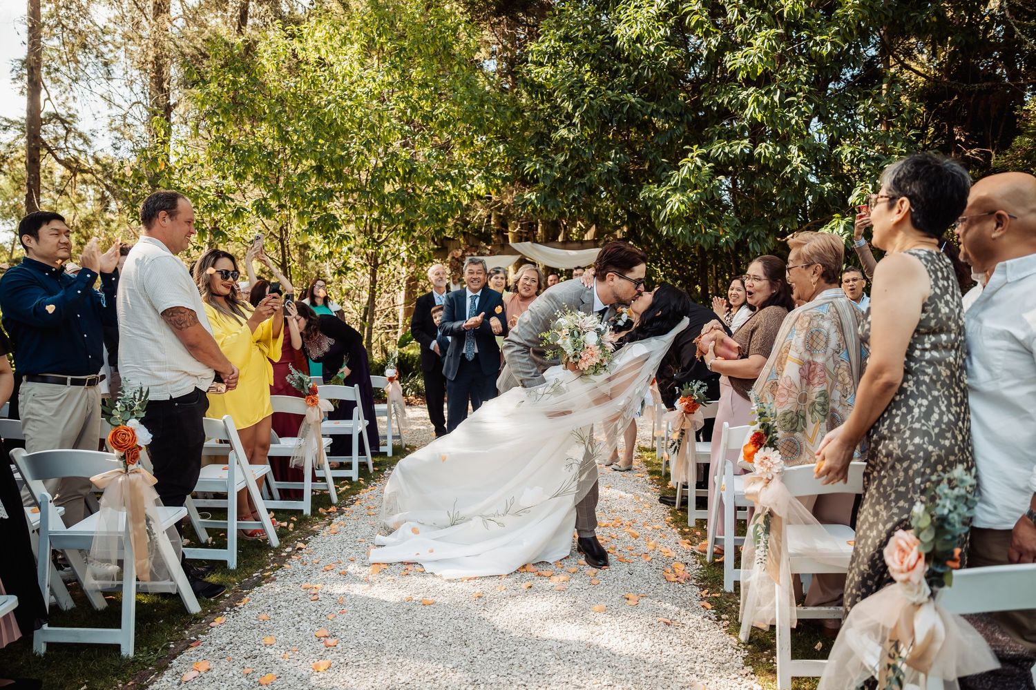 Bride and groom share a dip kiss while walking down the aisle at an outdoor wedding ceremony.