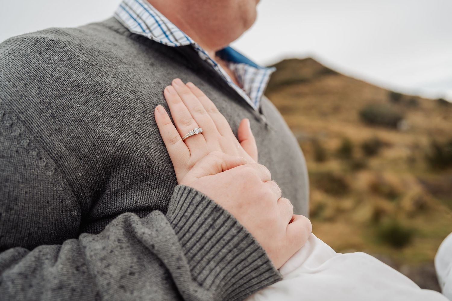 Couples engagement photography session in brown mountainous landscape with person wearing checkered shirt and sweater.