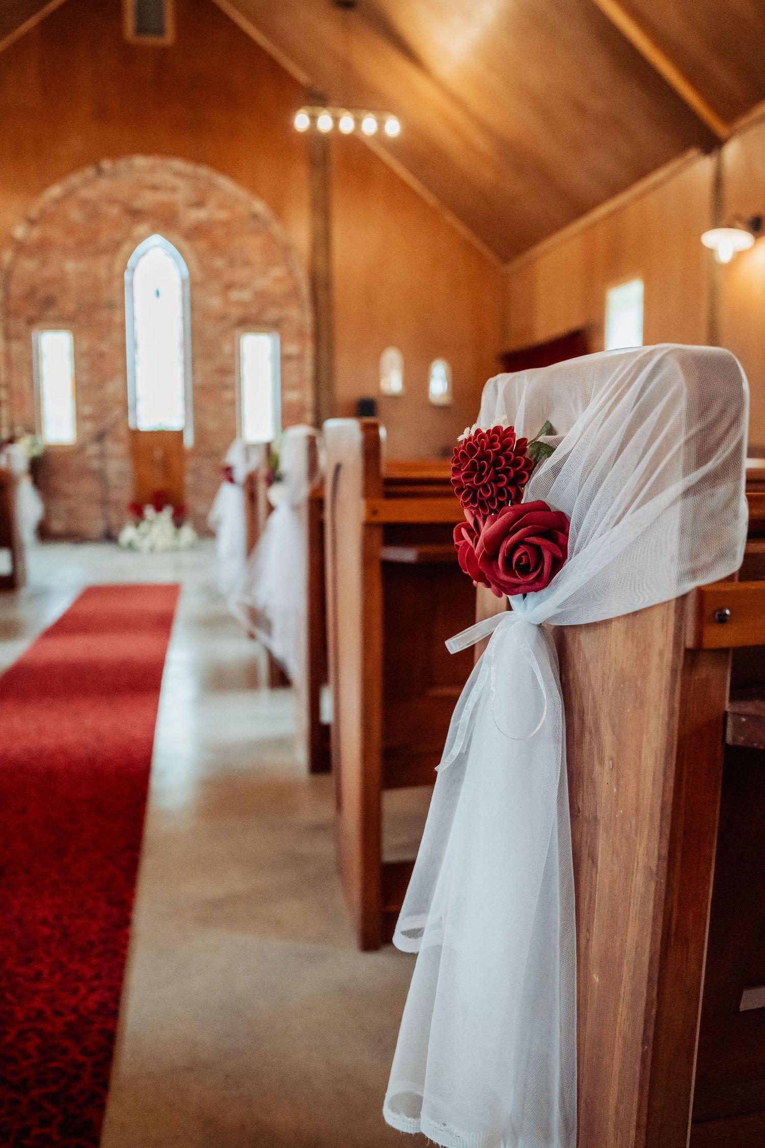 Church pew decorated with white tulle and red roses for a wedding ceremony.