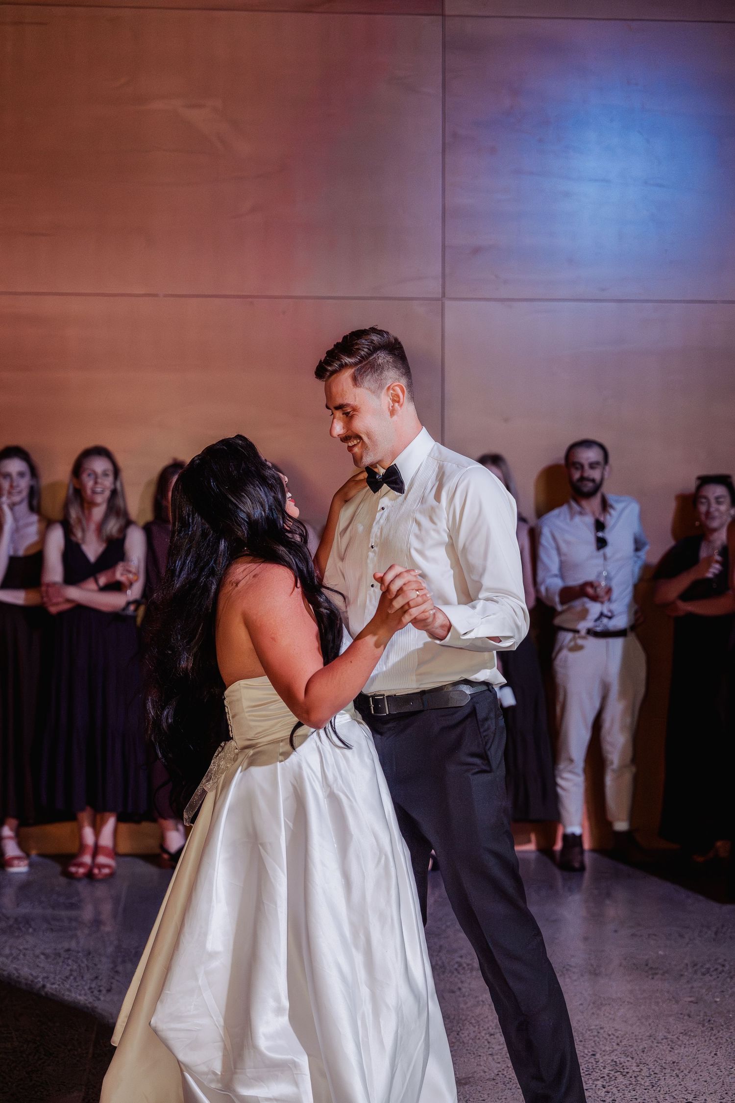 Bride and groom sharing their first dance while wedding guests watch in warmly lit reception venue.