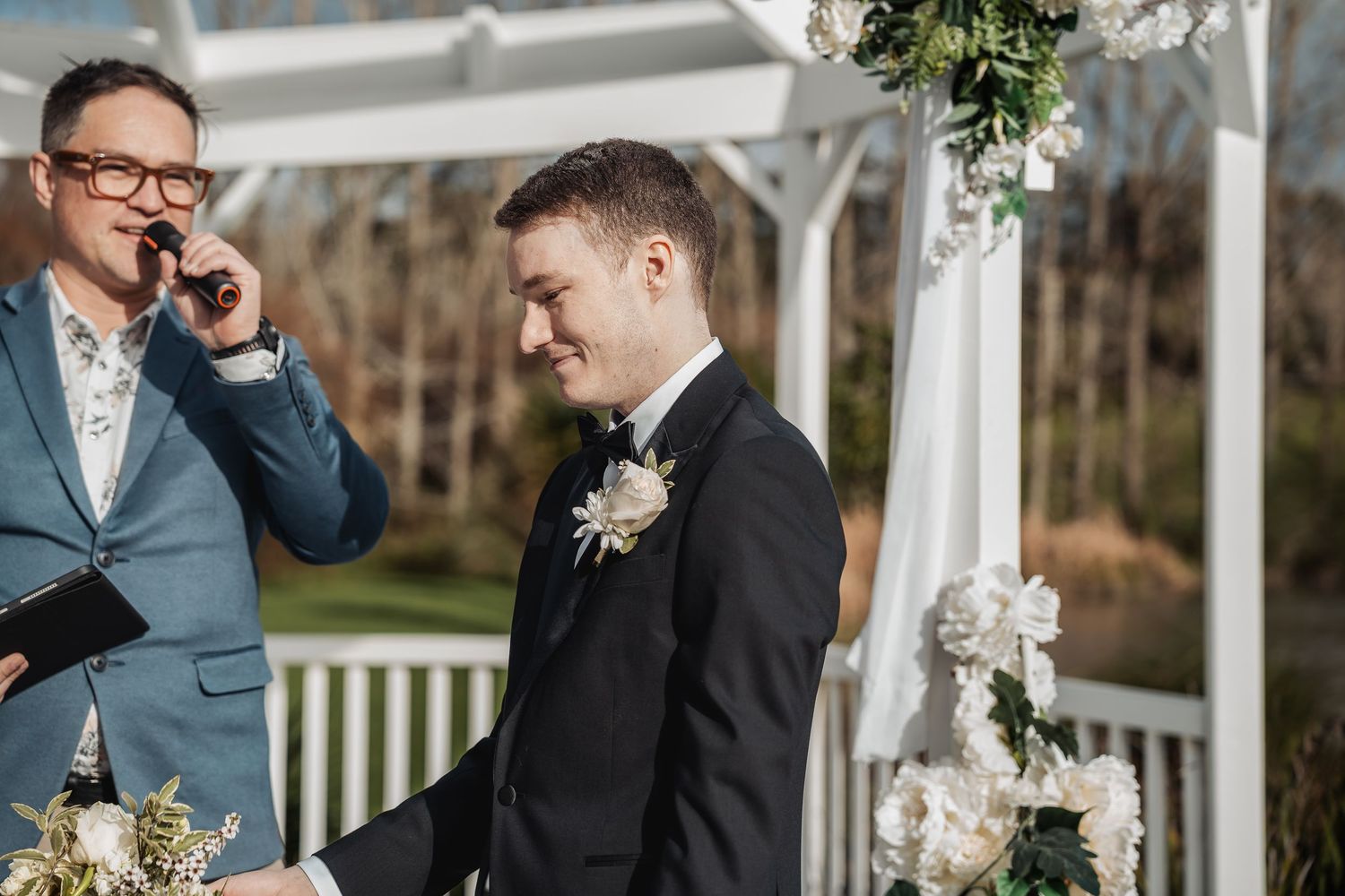 A couple shares a joyful moment during their wedding ceremony beneath a white gazebo with floral decorations.
