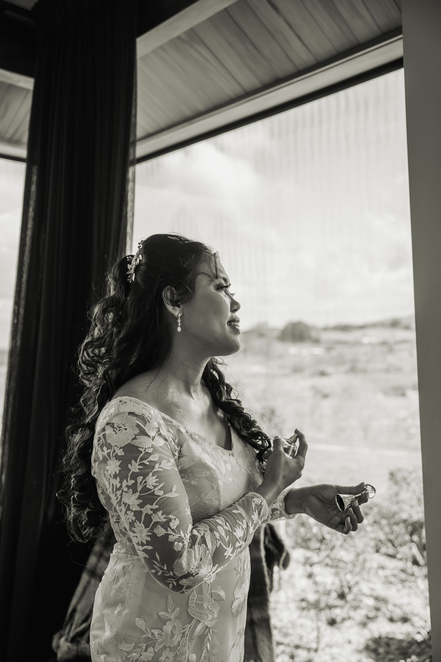 Black and white portrait of a bride looking up by a window in natural light.