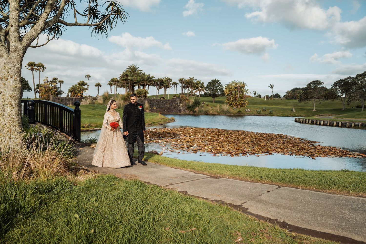 Wedding party walks along scenic coastal path with palm trees and water views.