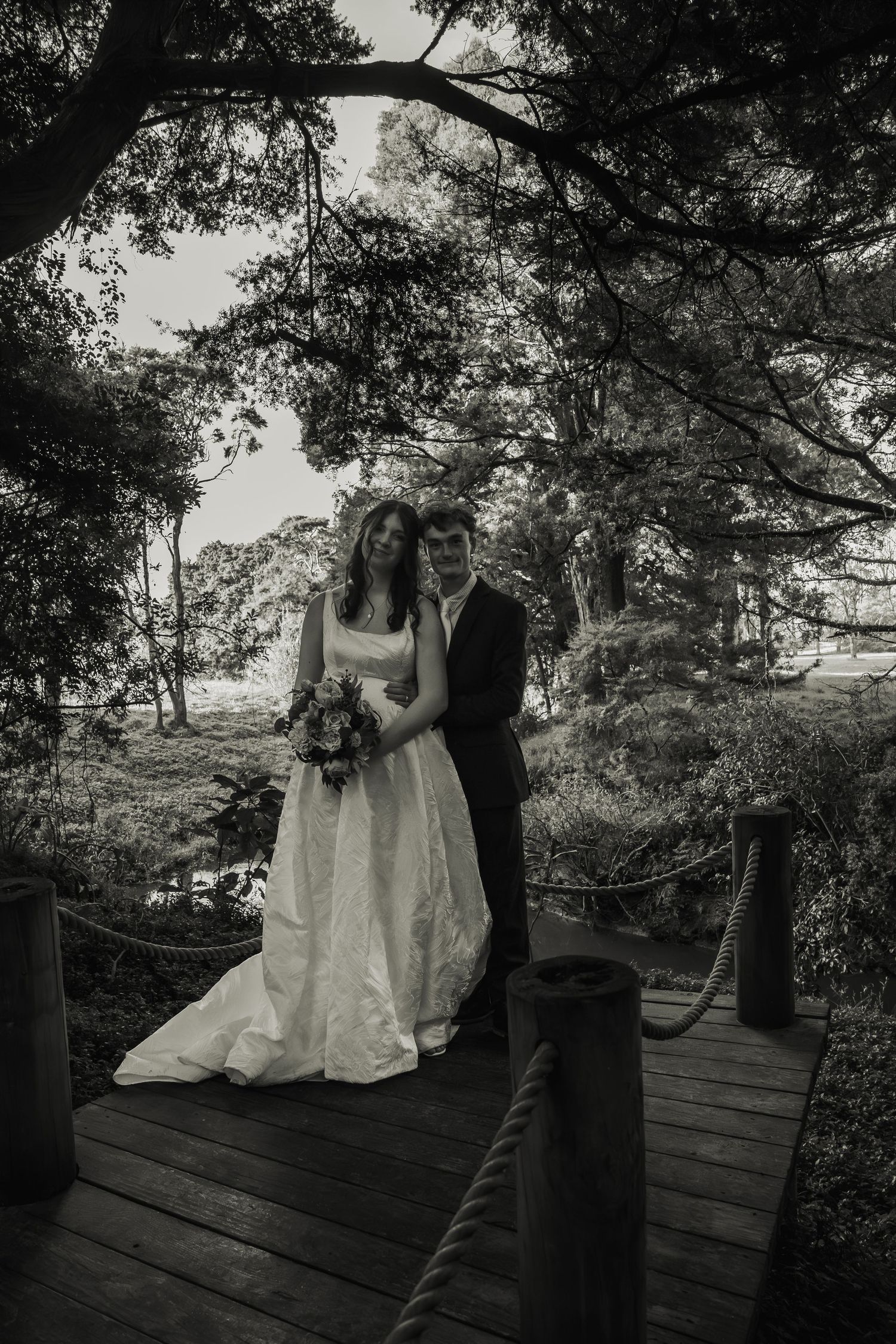 Black and white photo of bride and groom on wooden deck surrounded by trees.