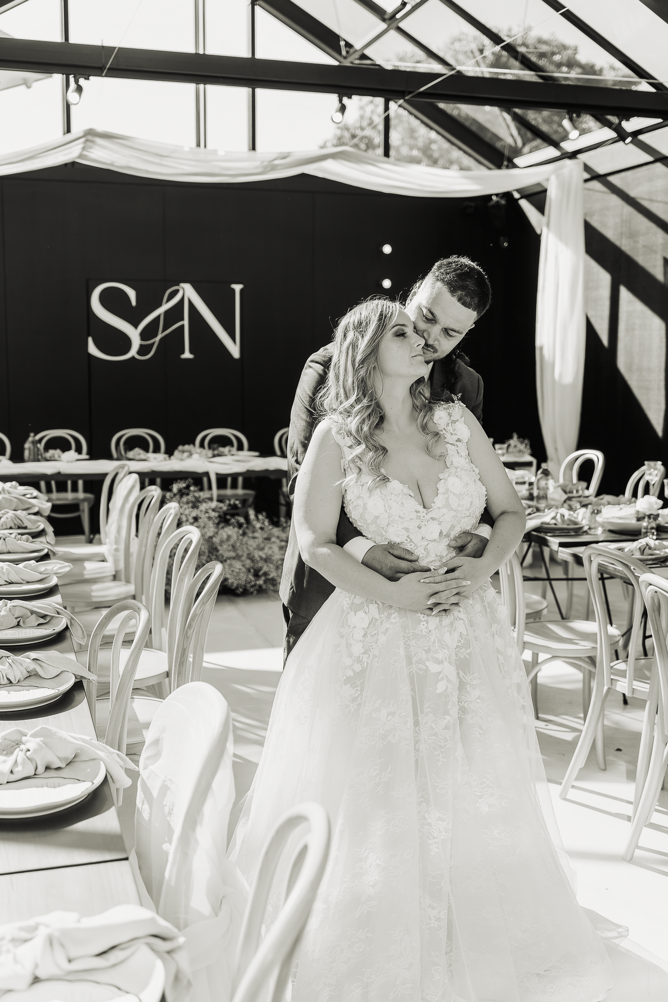 Black and white indoor wedding photo at venue with SAN logo backdrop.