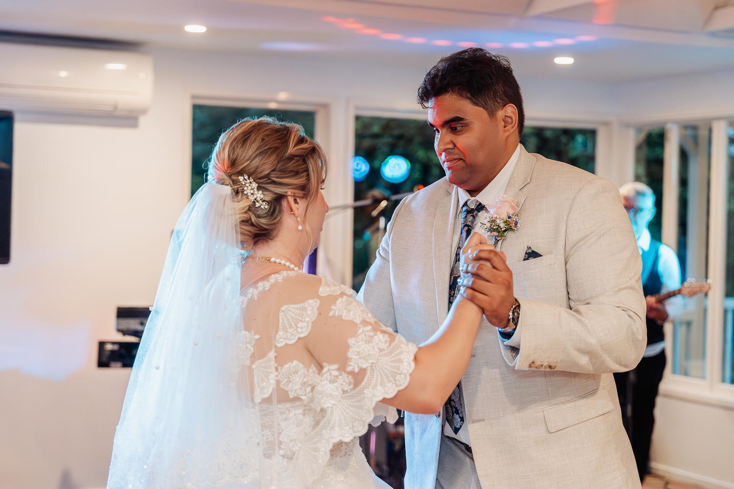 Close-up of a wedding couple's first dance showing the bride's lace details and groom's cream suit.
