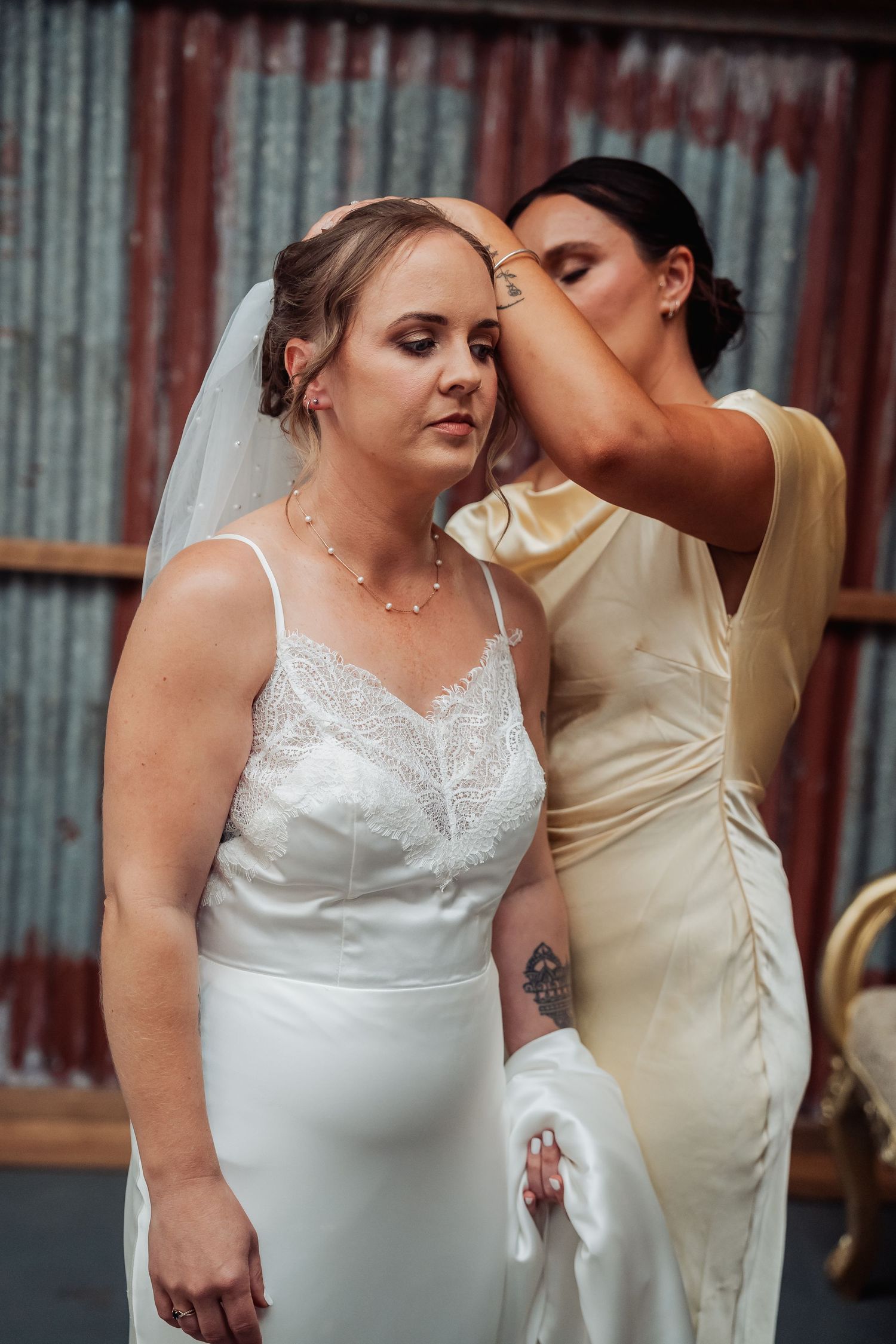Bridesmaid adjusting the veil of a bride in a white lace wedding dress before the ceremony.