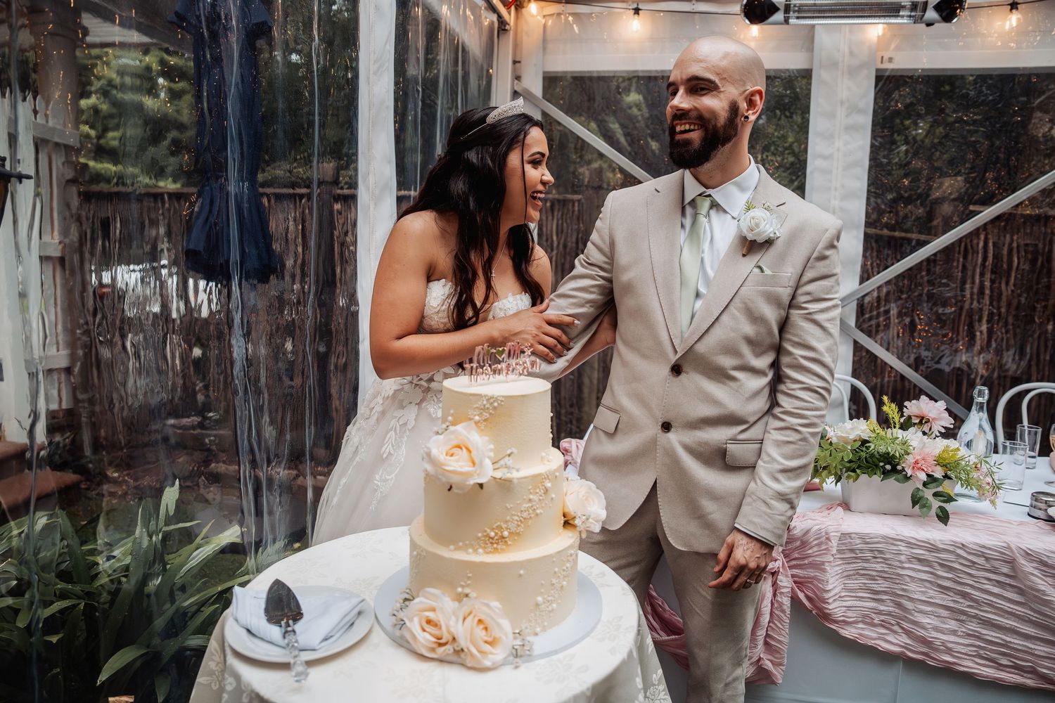 Happy couple cutting three-tier white wedding cake at elegant reception celebration.