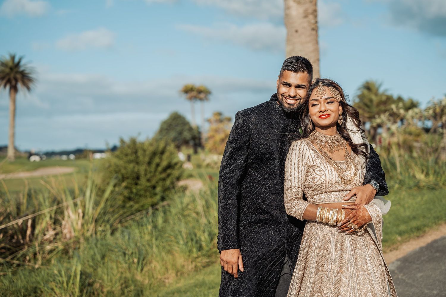 A romantic photoshoot on a palm-tree lined path with coastal scenery in the background.