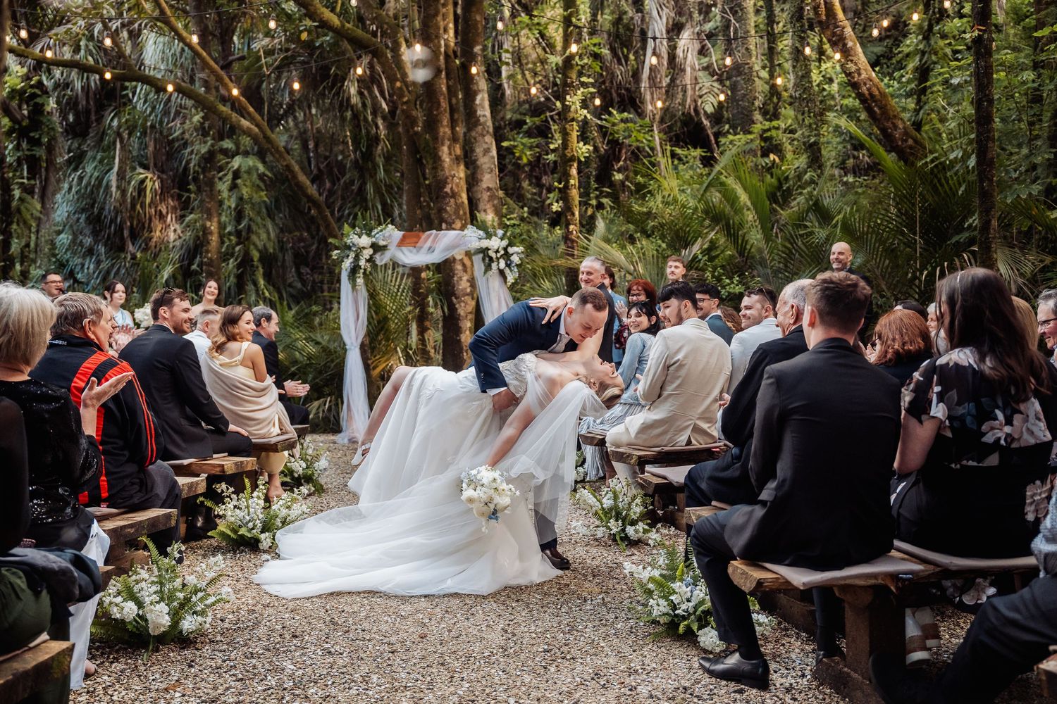 Wedding guests seated during outdoor forest ceremony with natural light filtering through trees.