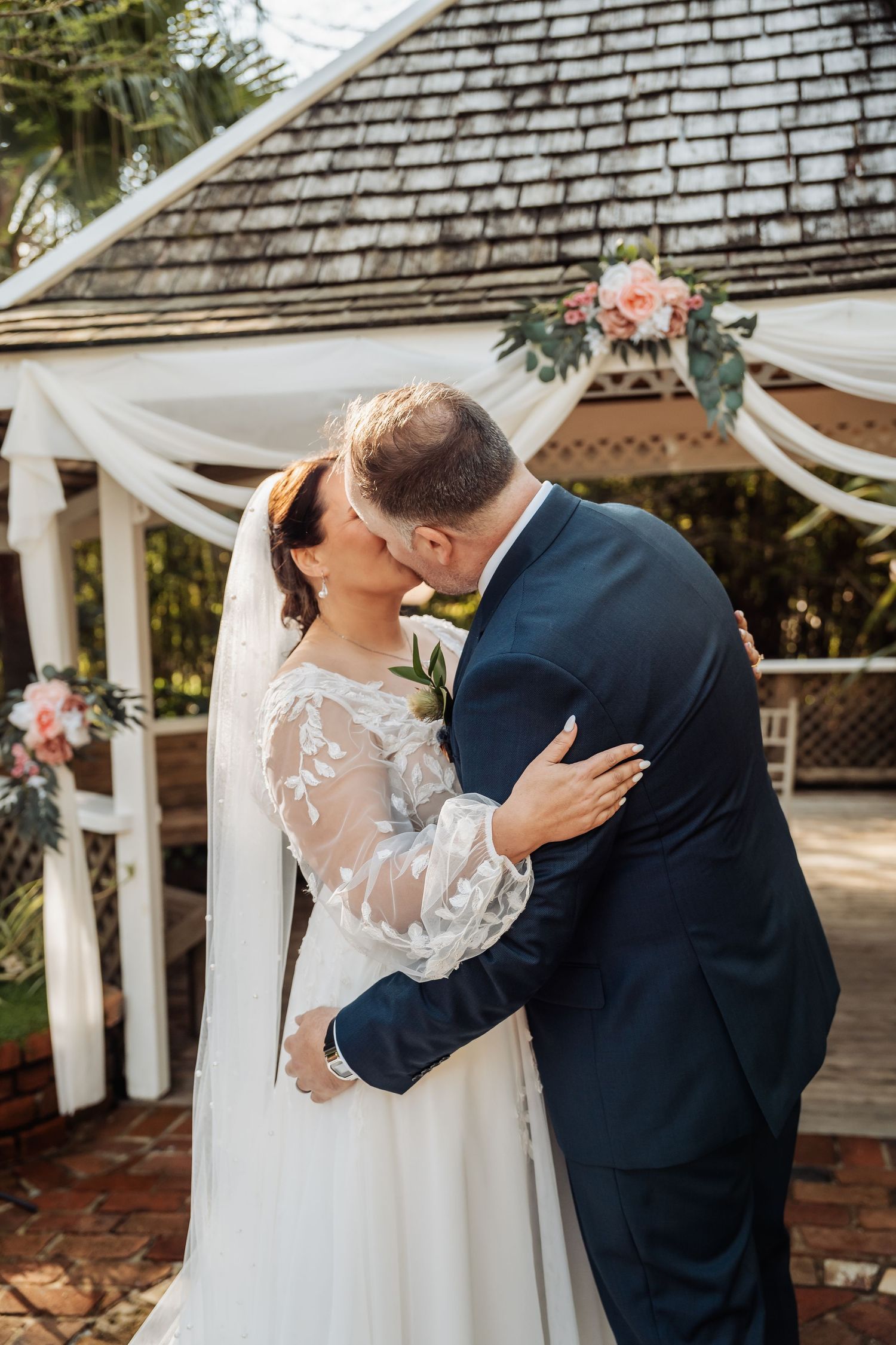 Romantic wedding couple sharing a moment under a shingled gazebo.