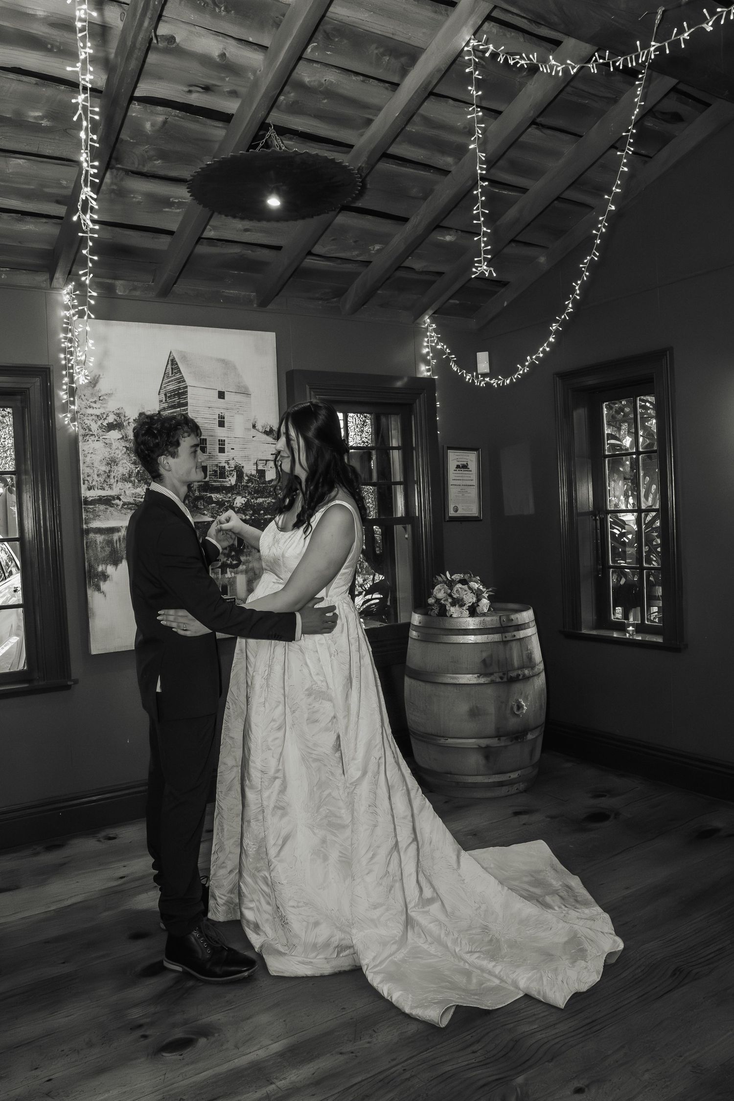 Black and white photo of bride and groom sharing first dance in rustic venue.