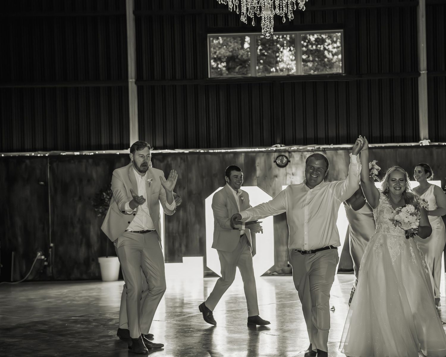 Black and white photo of groomsmen dancing energetically on barn dance floor during wedding reception.