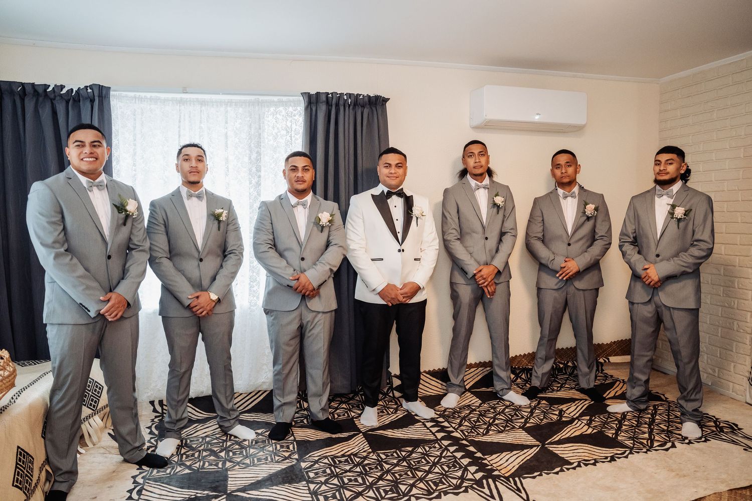 Groomsmen in matching light gray suits and pink ties pose together in a modern room.
