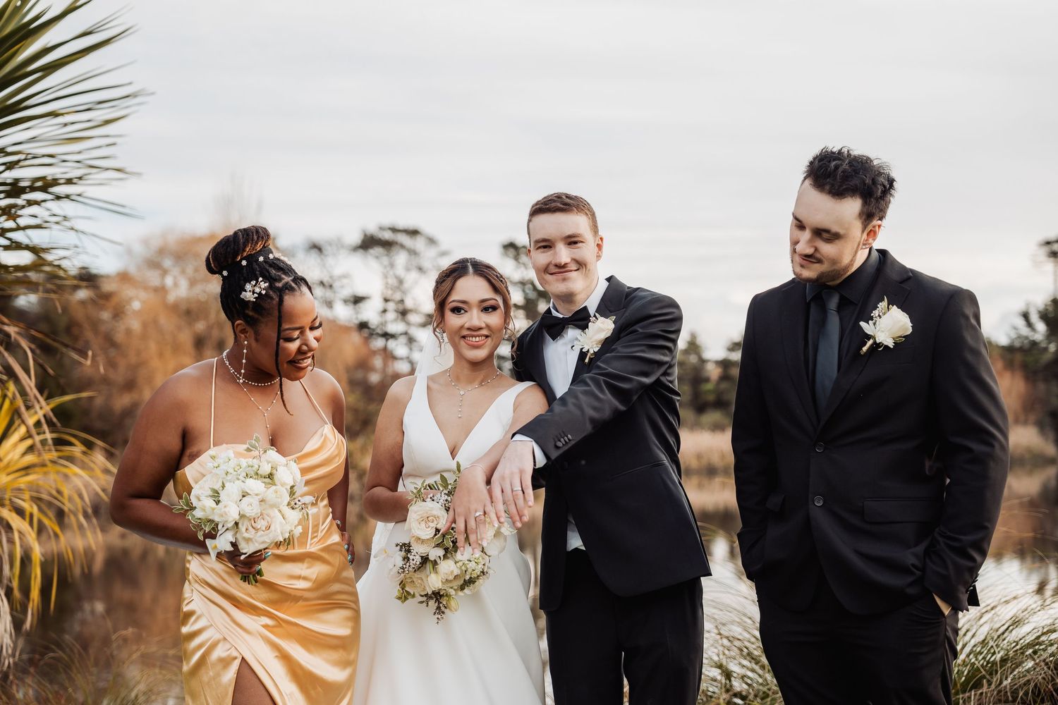 Wedding party poses together in formal attire against a natural outdoor backdrop.