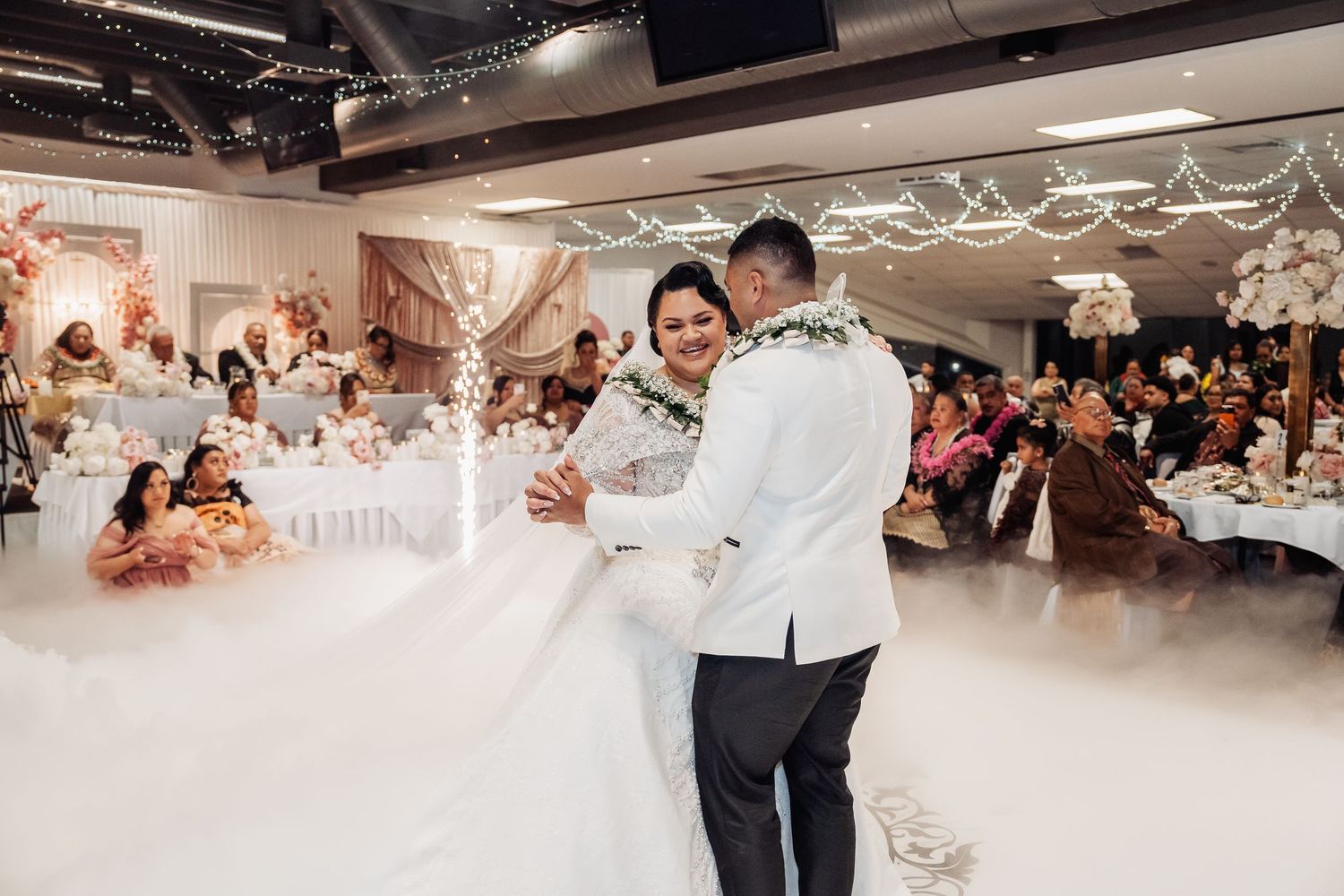 Reception venue with white decor showing wedding celebration and dancing guests.