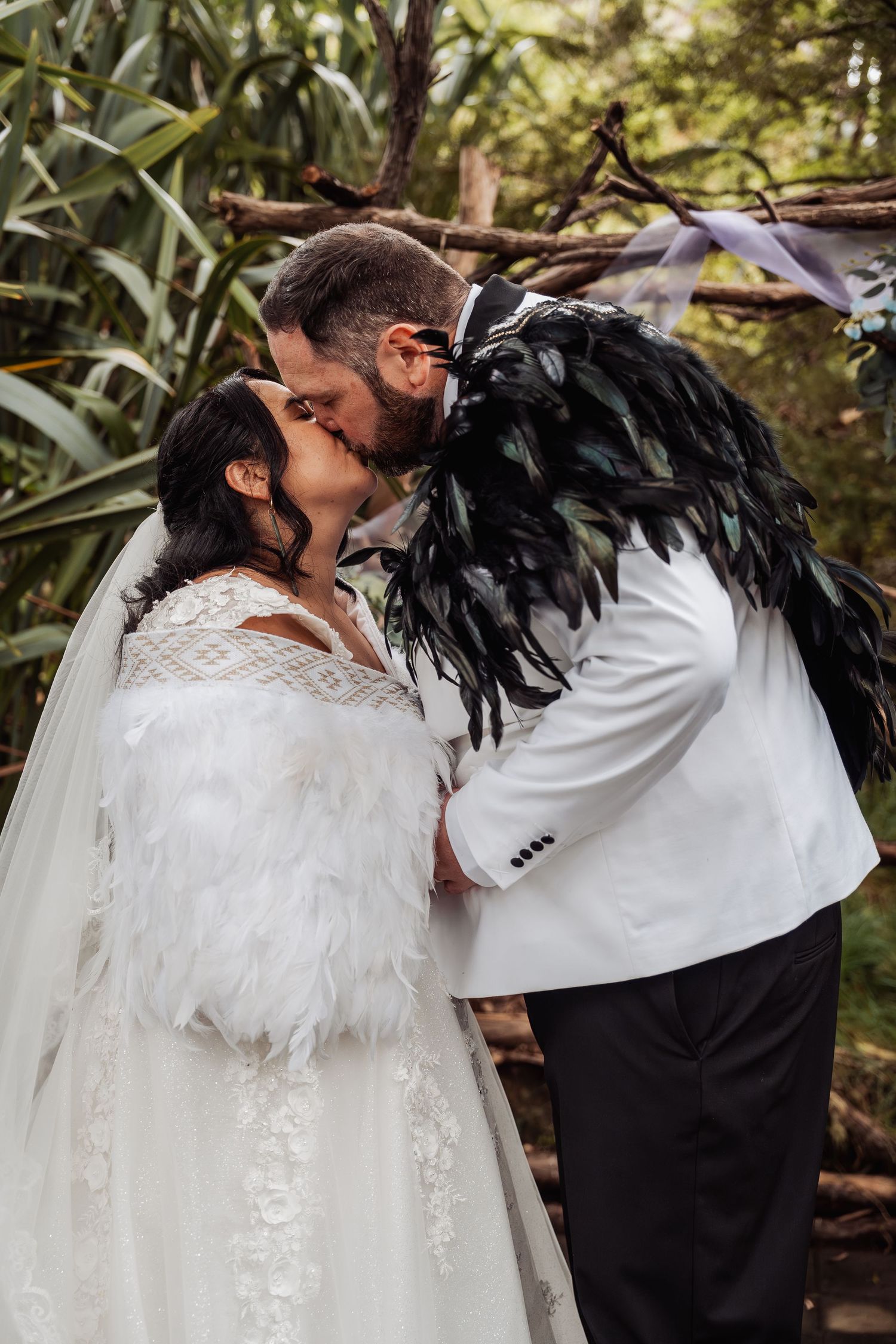 Bride and groom share their first kiss surrounded by lush greenery at outdoor wedding.