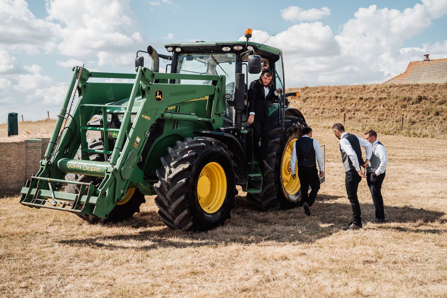 Men in formal attire inspecting a green John Deere tractor in a harvested field on a sunny day.