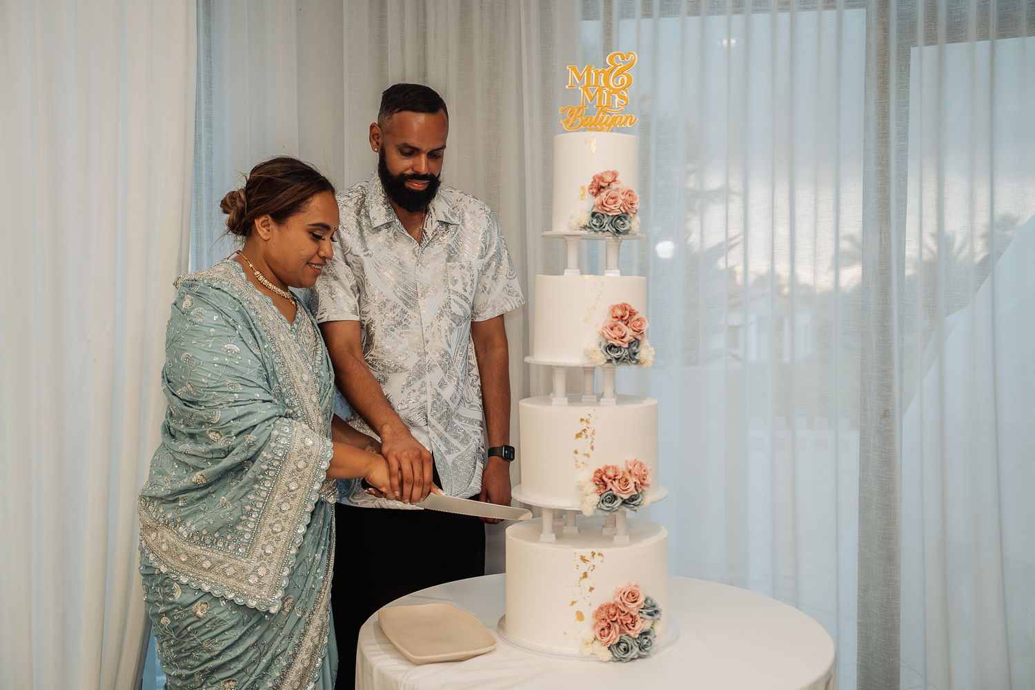 A couple cutting their elegant four-tier wedding cake decorated with peach flowers.