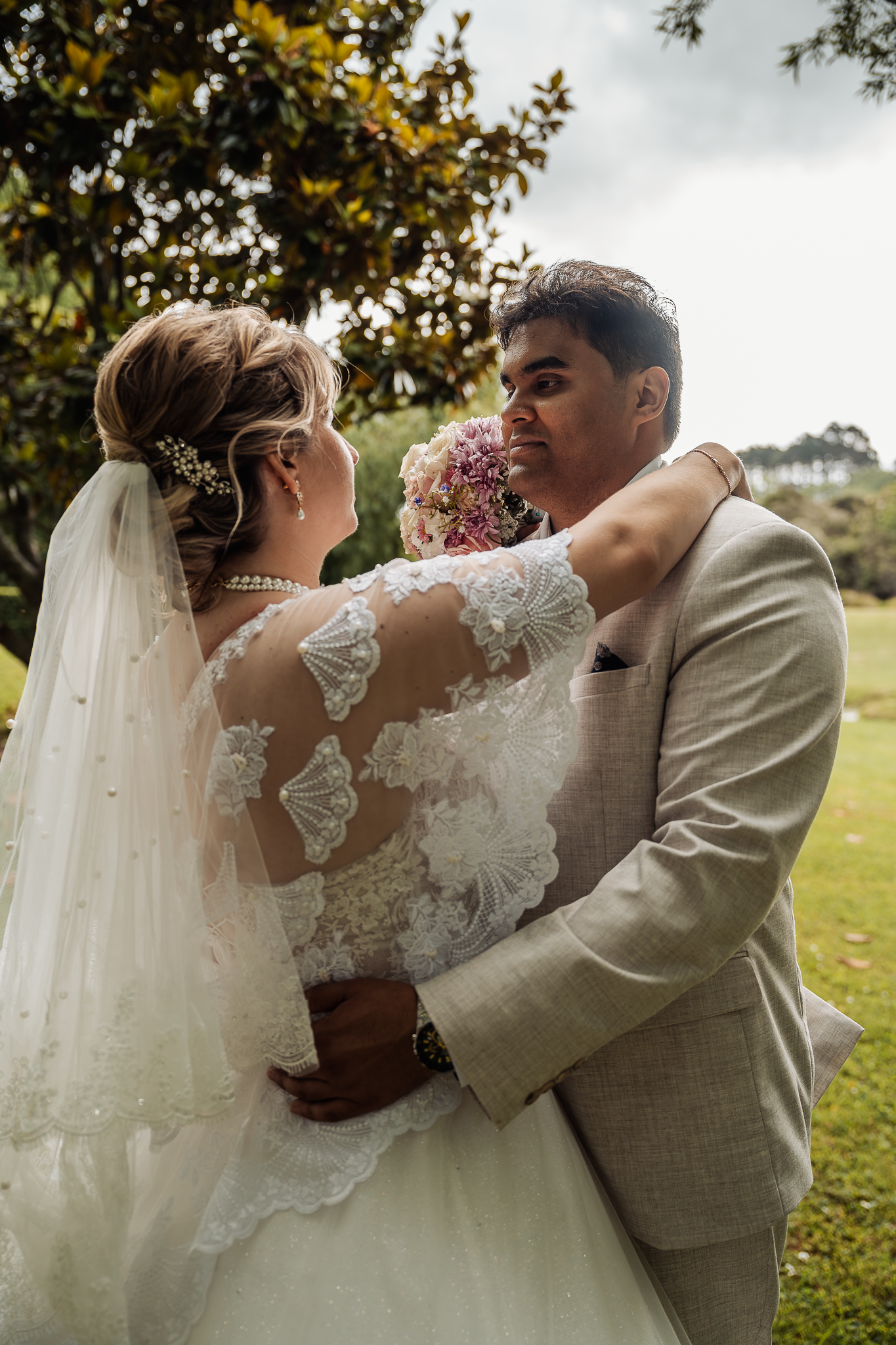 Close-up of tender wedding moment in sunlit garden with magnolia trees.