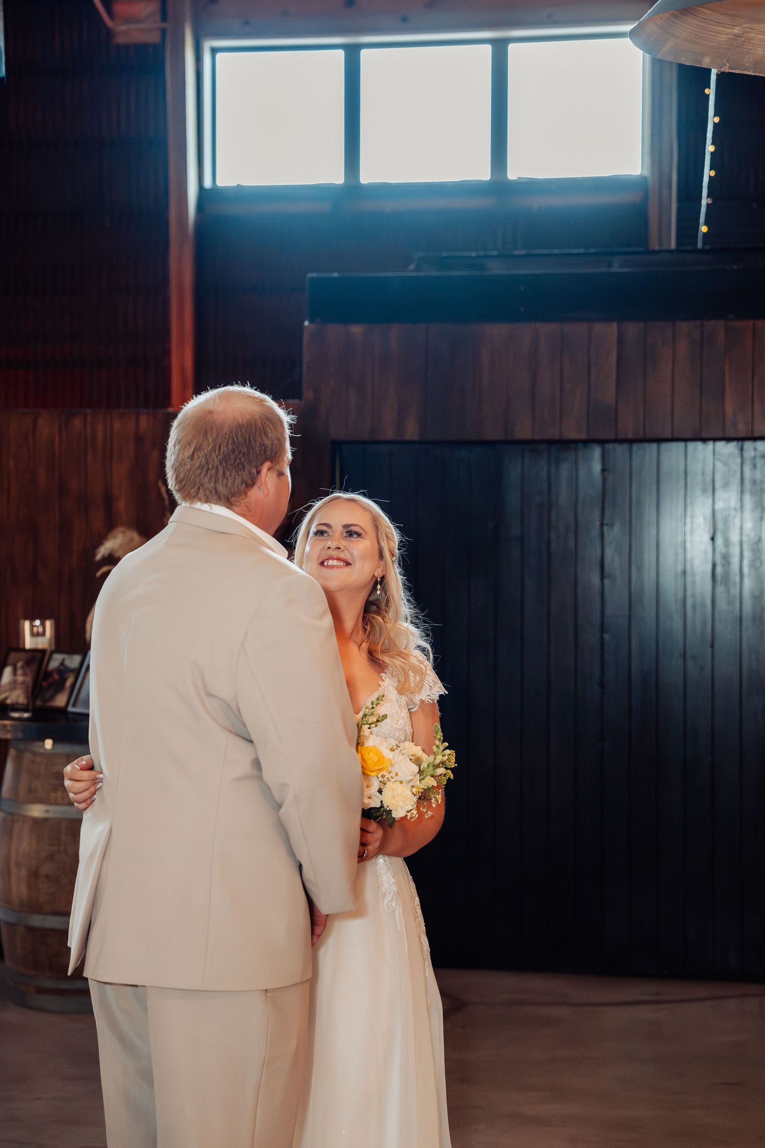 Bride smiling at groom during first dance in rustic barn wedding venue.
