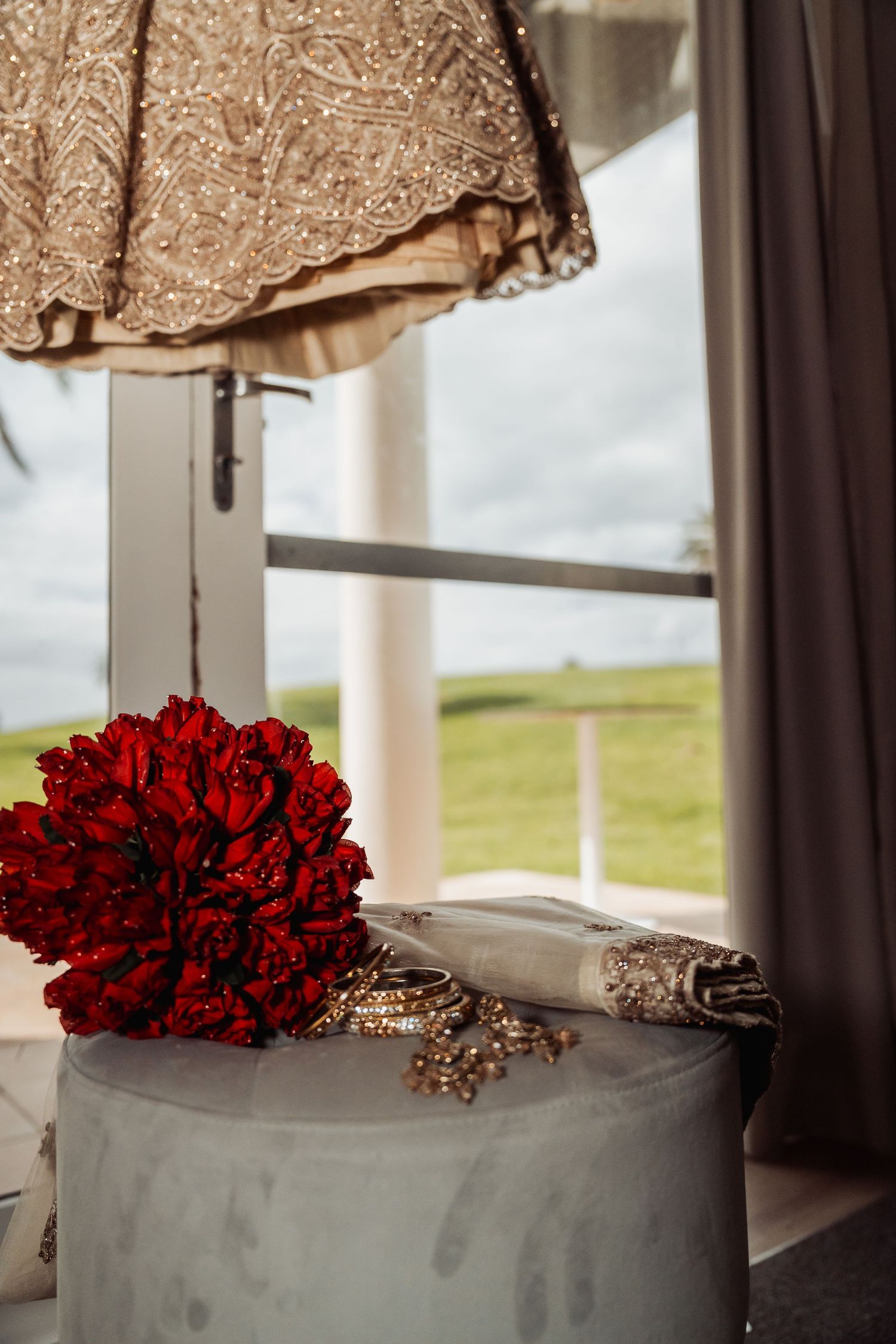 Elegant wedding cake with deep red rose bouquet topper displayed by window with countryside view.