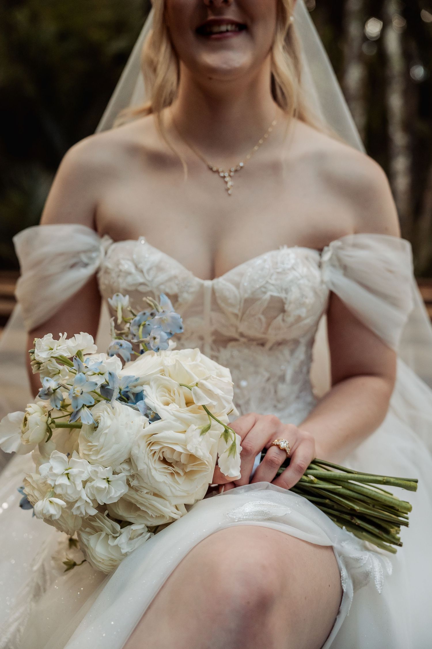 A detailed shot of a white bridal bouquet with blue accents against an elegant wedding dress.