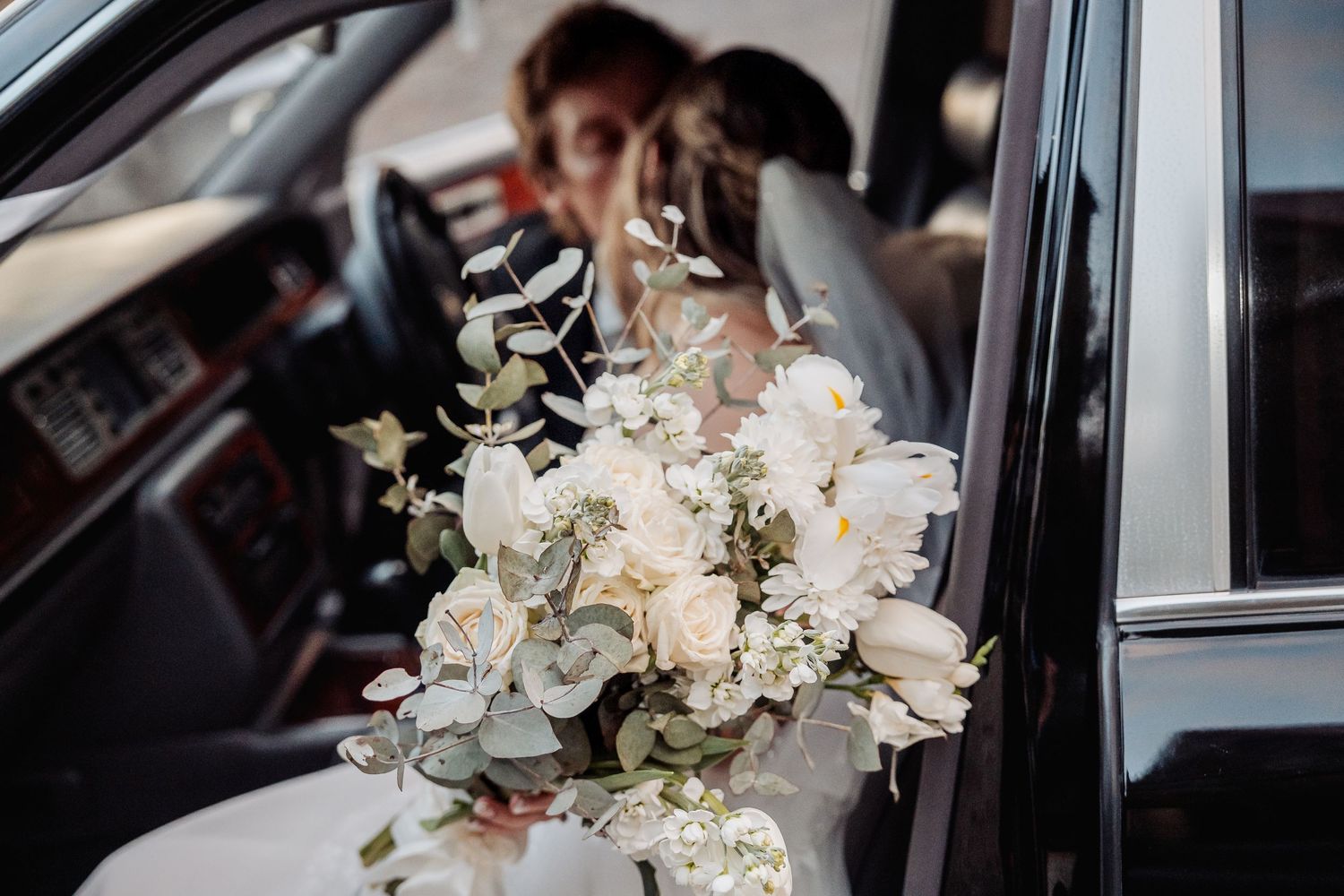 A beautiful white and green bridal bouquet rests in a car featuring orchids and delicate foliage.
