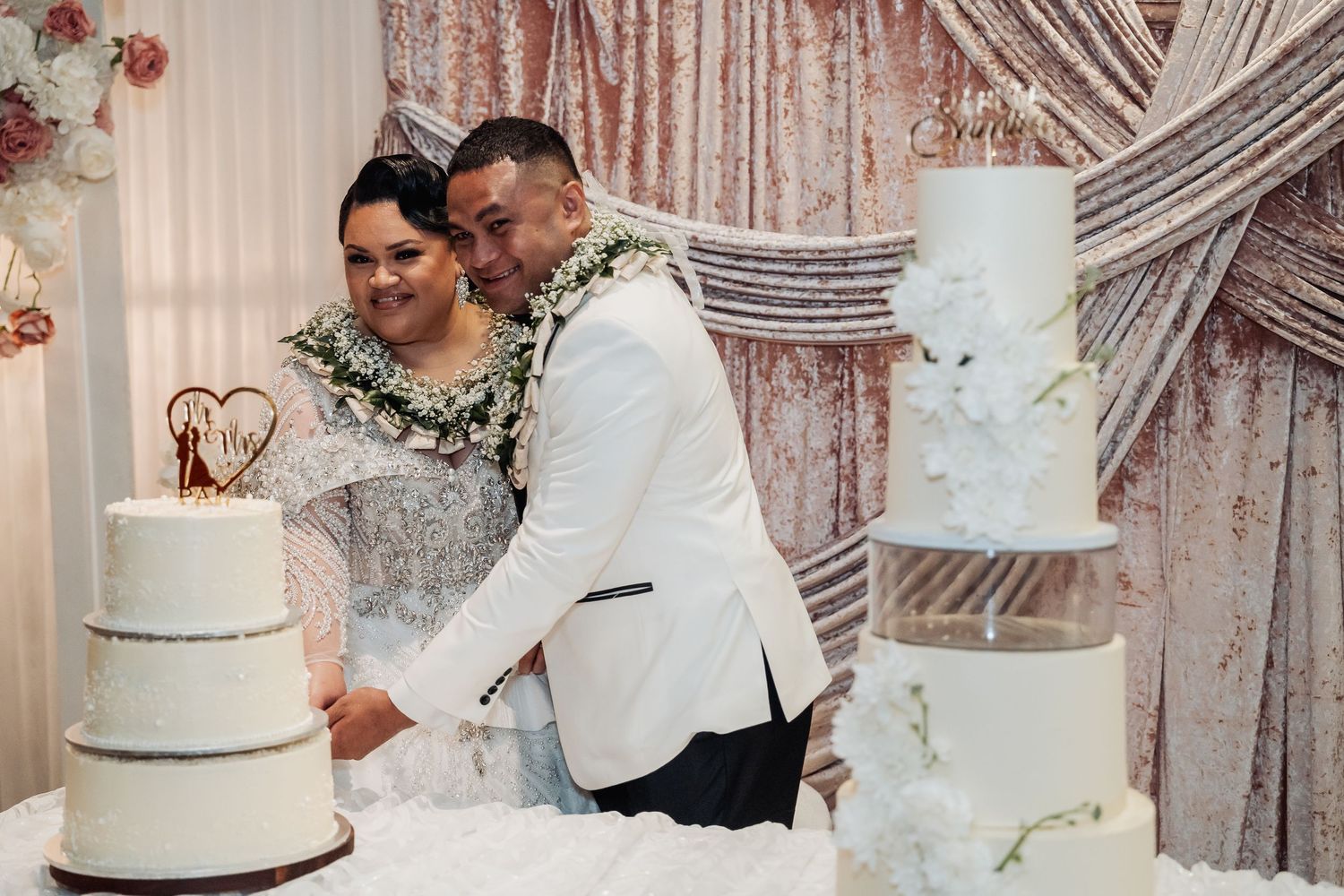 Elegant white and silver wedding cakes displayed against rose gold sequin backdrop.