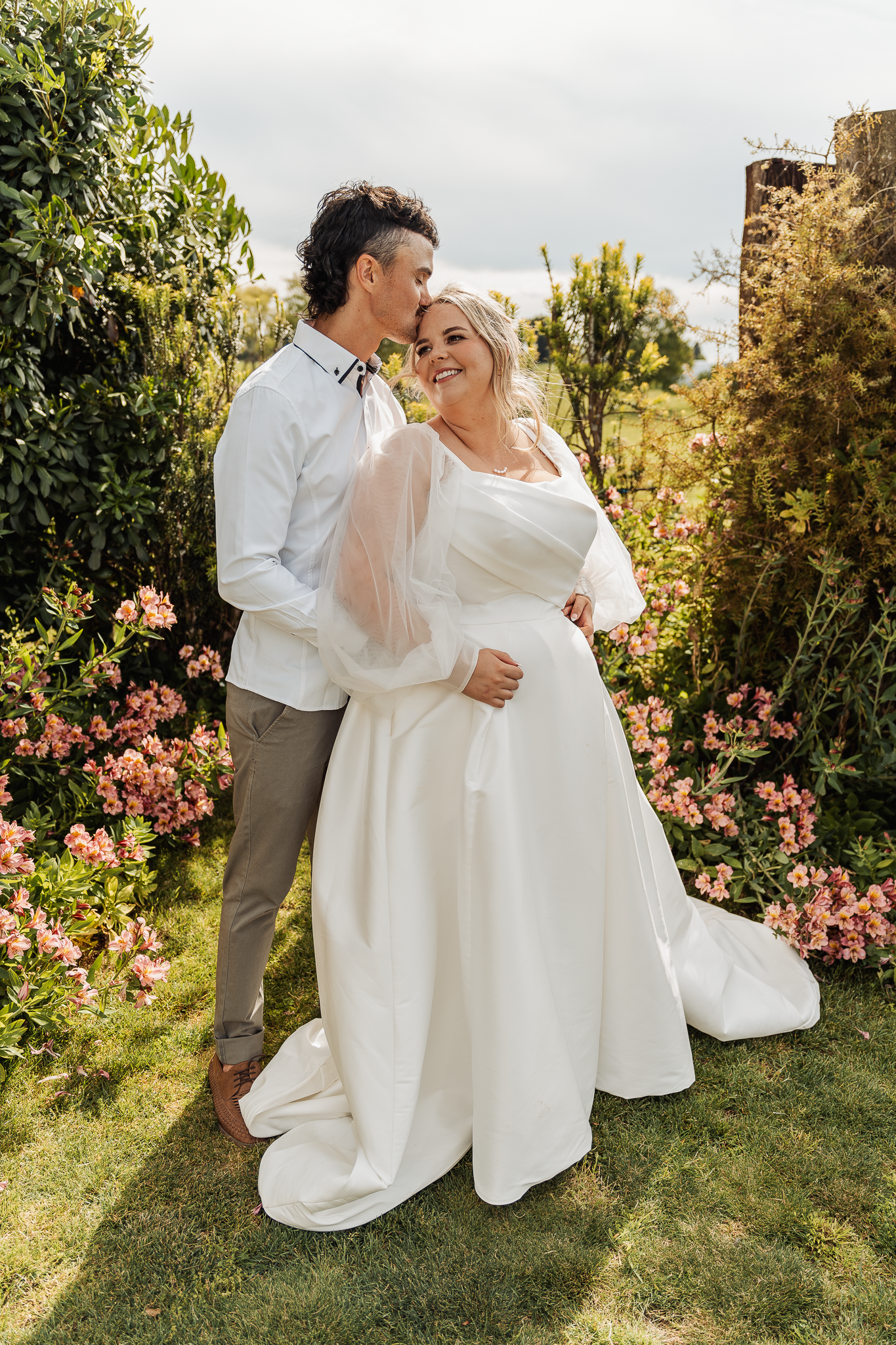 Romantic wedding couple embracing in a garden with blooming pink flowers.