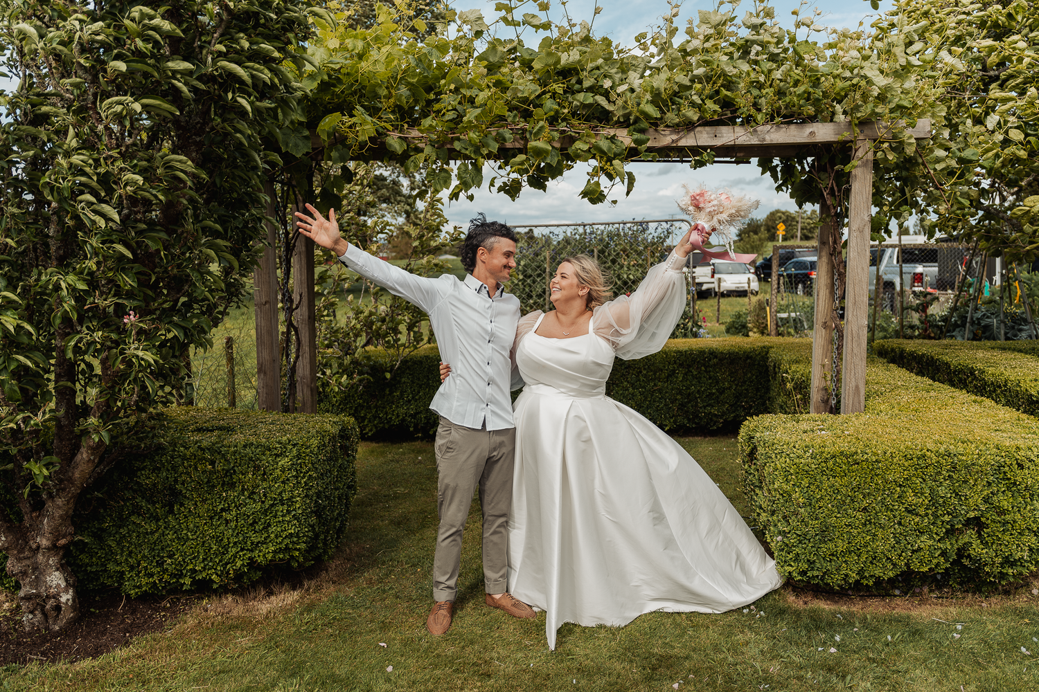 Joyful couple celebrating under a wooden archway in a garden setting with lush greenery.