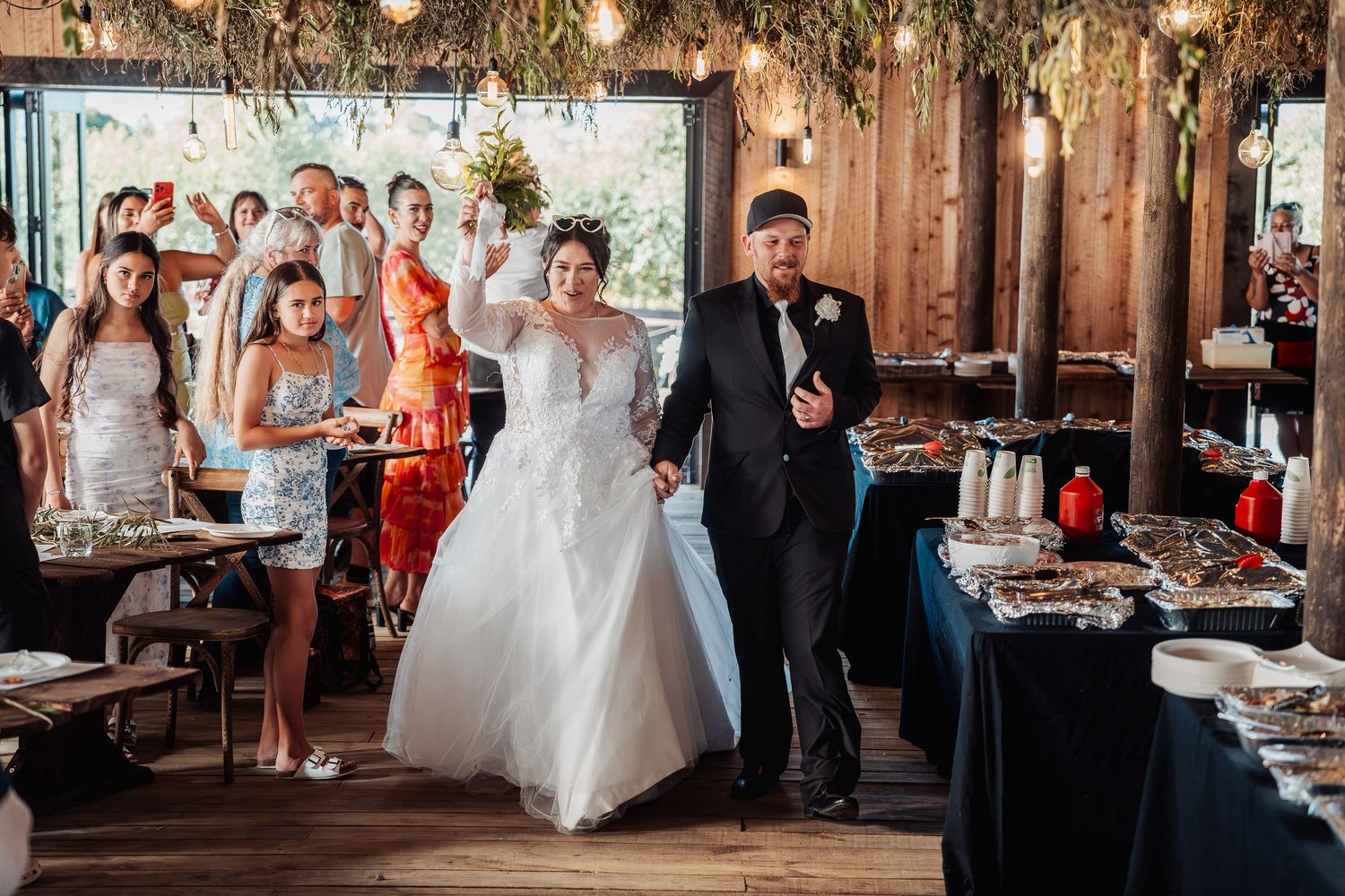 Wedding celebration in rustic wooden venue with guests cheering during reception festivities.
