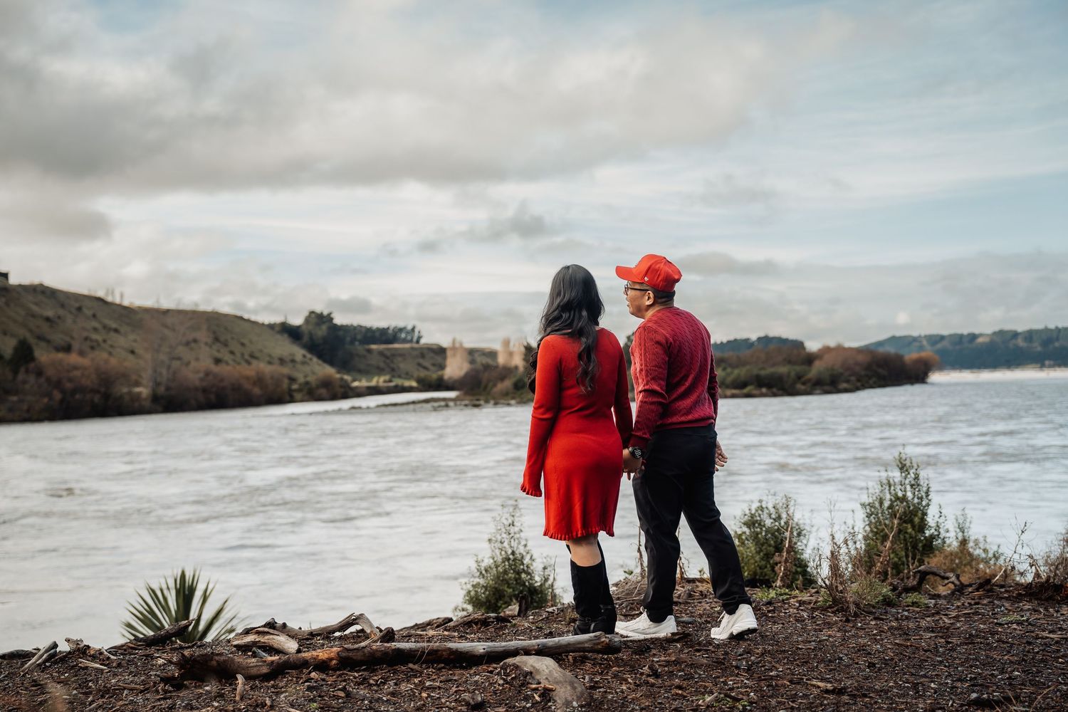 Couple in matching red outfits holding hands while gazing at a scenic coastal view on a cloudy day.