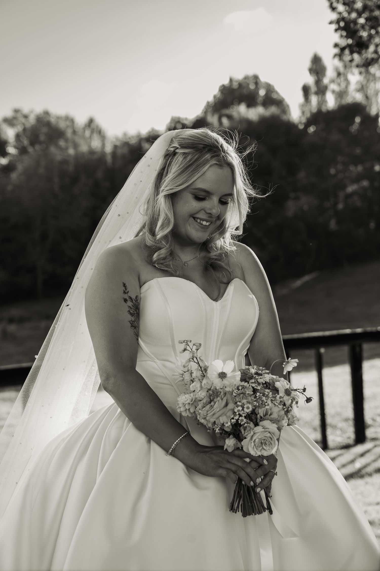 A black and white portrait of a bride in a strapless ballgown holding a floral bouquet with a gentle smile.