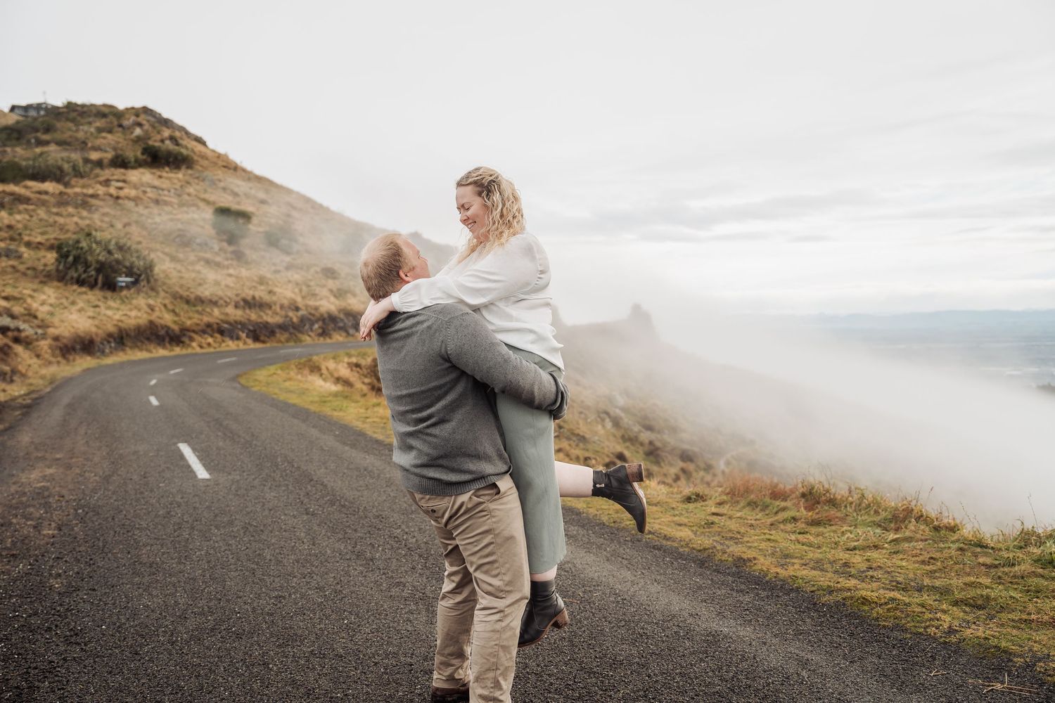 Car driving on scenic mountain road along foggy coastal cliffs with dramatic ocean views.