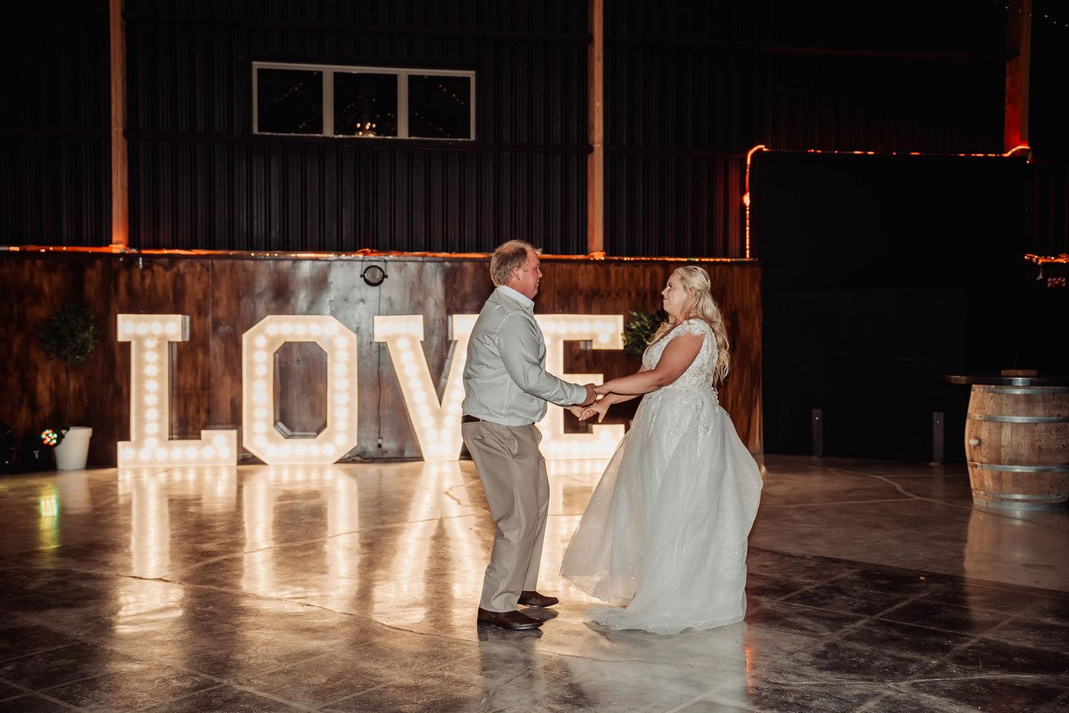 Bride and groom share first dance in front of illuminated LOVE letters at wedding reception.