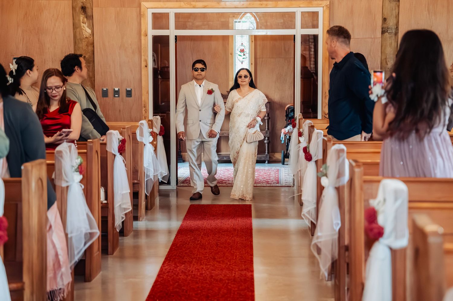 Bride and groom walking down the red carpet aisle of a wooden chapel during their wedding ceremony.