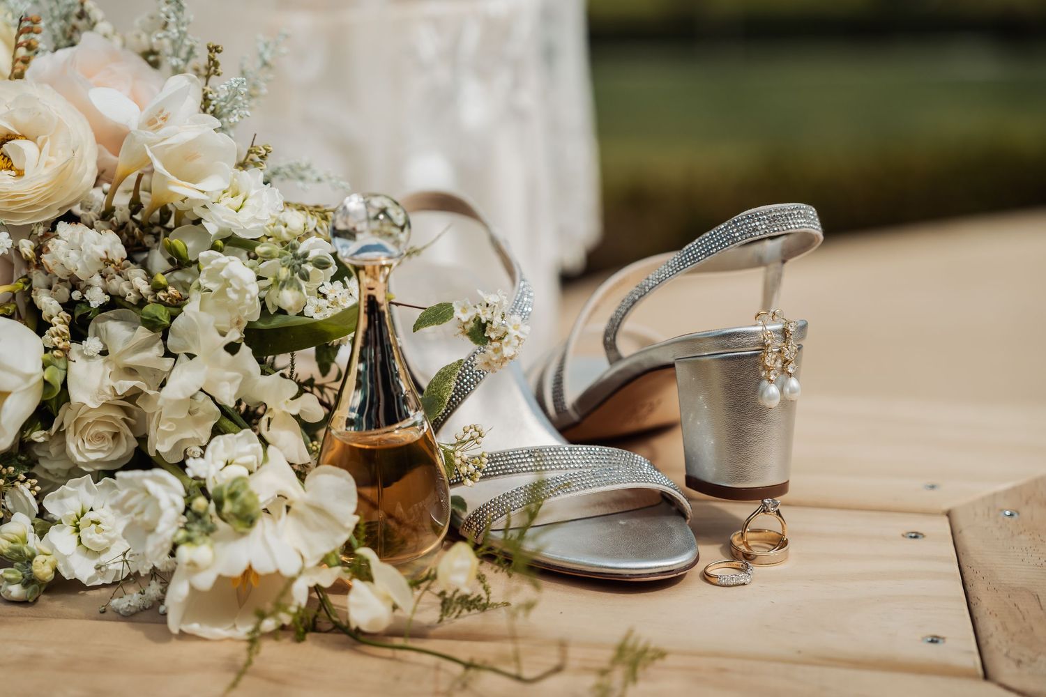 Elegant wedding details including white floral bouquets, silver shoes, and delicate decor arranged on a wooden surface.