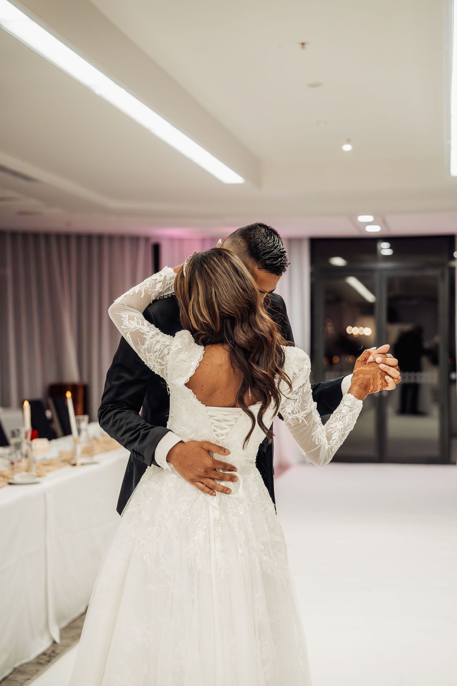 Newlyweds share their first dance in an elegant white reception venue.