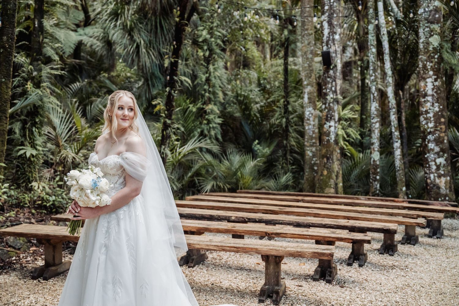 Elegant wedding scene in a forest clearing with wooden bench seating.