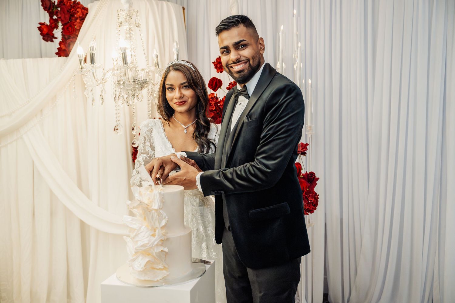 Wedding couple shares joyful moments against white backdrop with red roses.