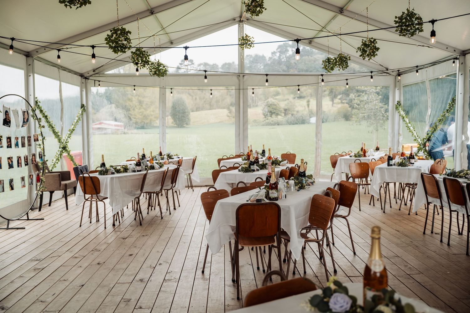 Elegant outdoor marquee wedding reception with white tablecloths, string lights, and green floral decorations.
