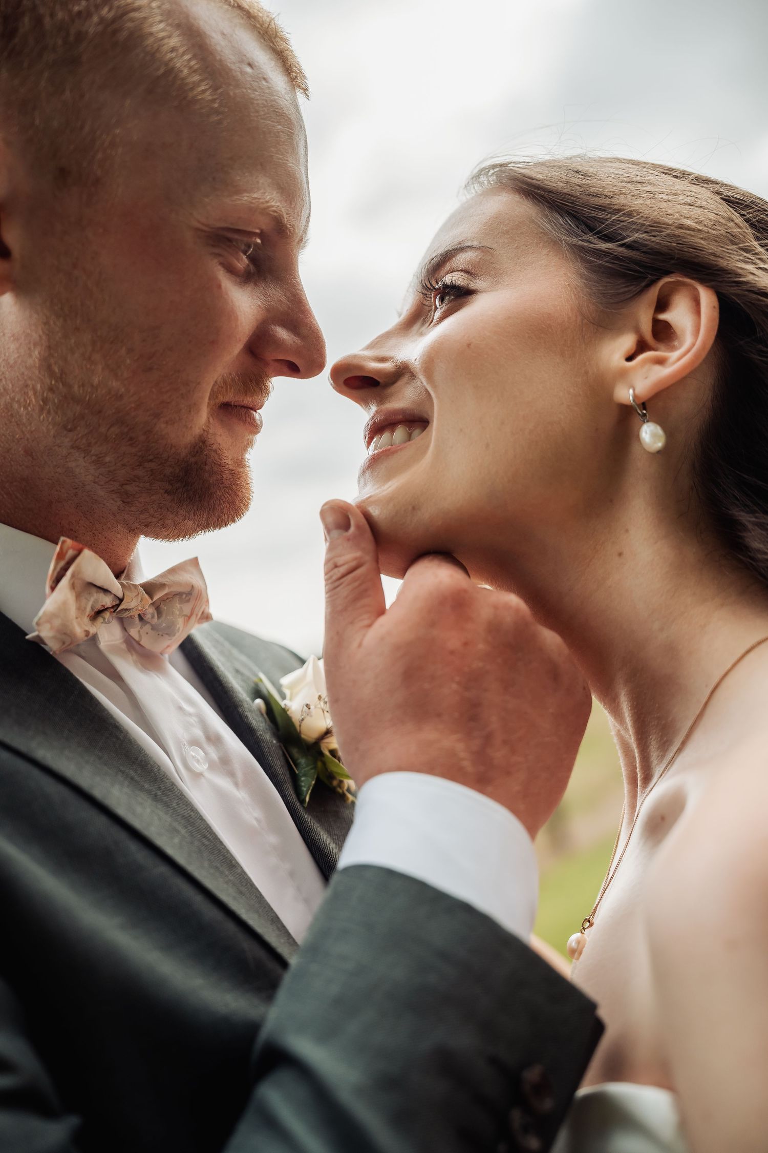 Close-up of groom gently holding bride's chin as they gaze lovingly at each other outdoors.