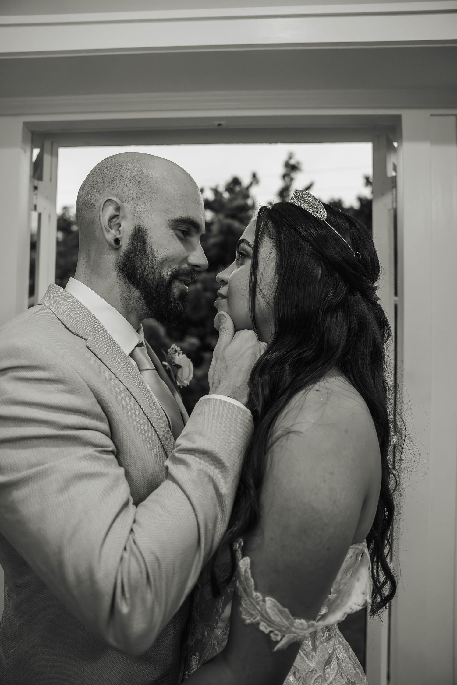 Black and white portrait of groom gently touching bride's face as they gaze at each other.