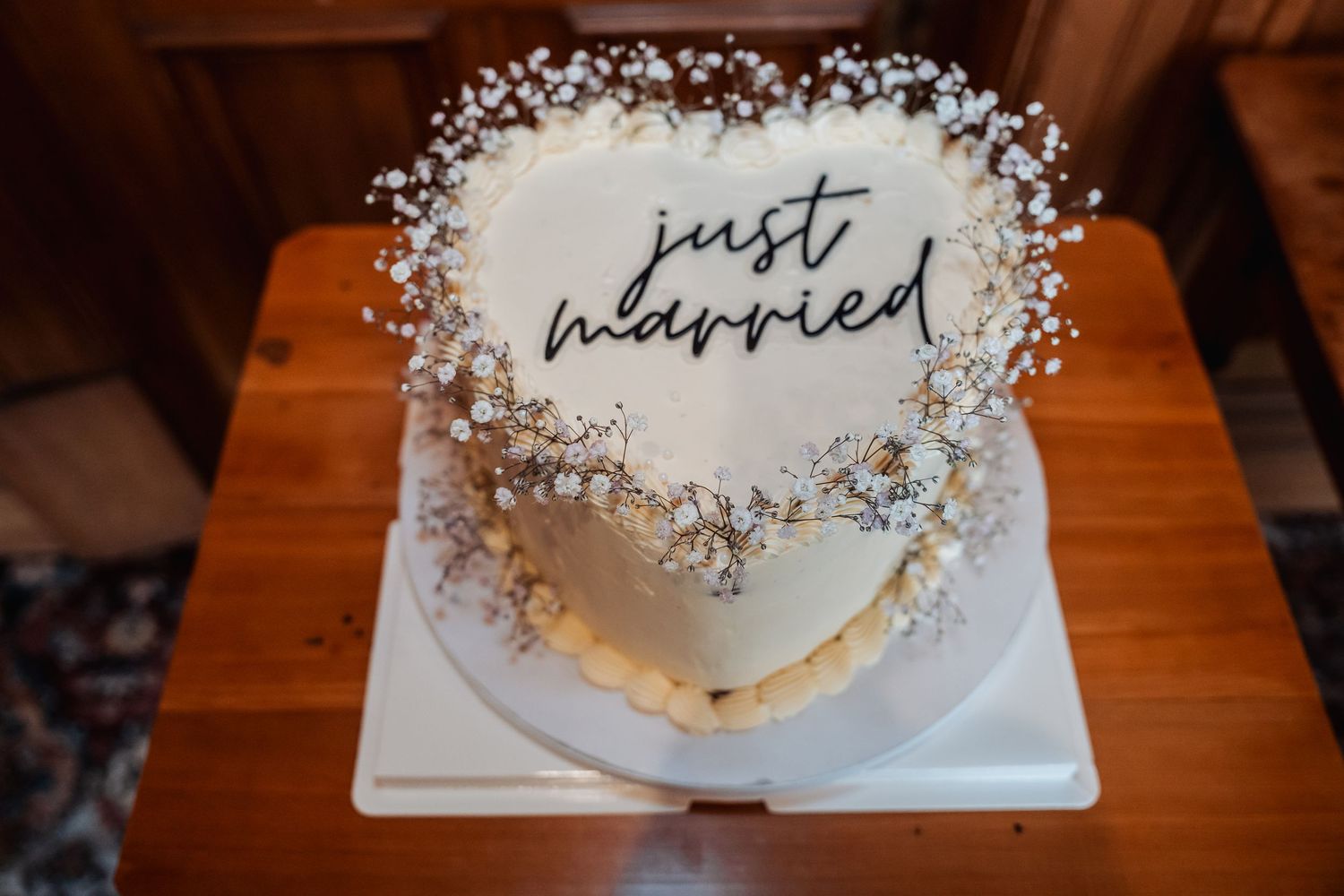 Heart-shaped white wedding cake decorated with baby's breath and just married script topper.