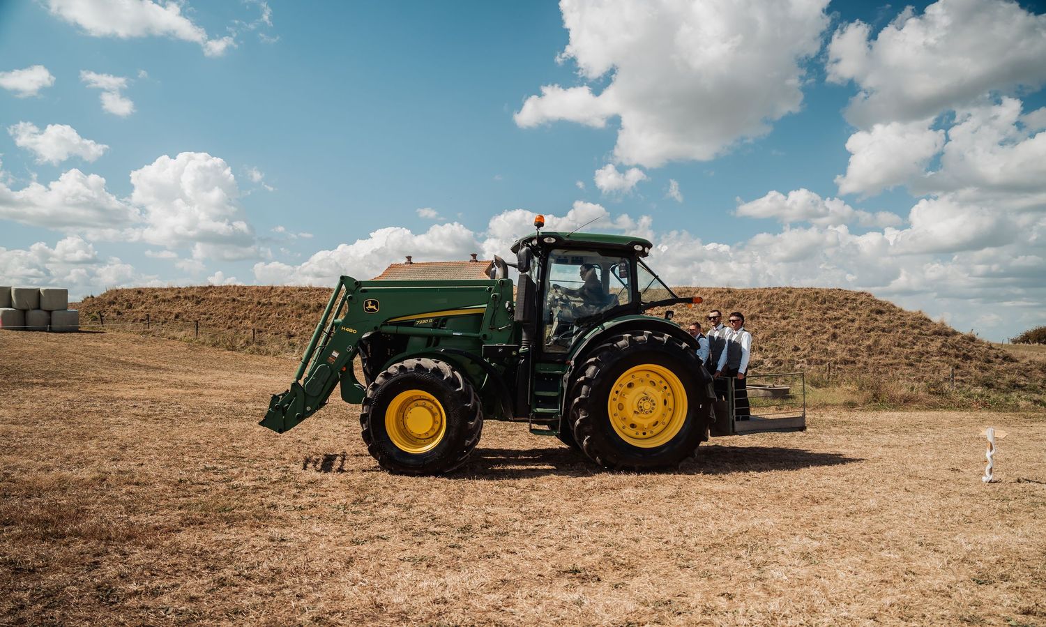 John Deere green tractor parked in a dry field under a blue sky with clouds.