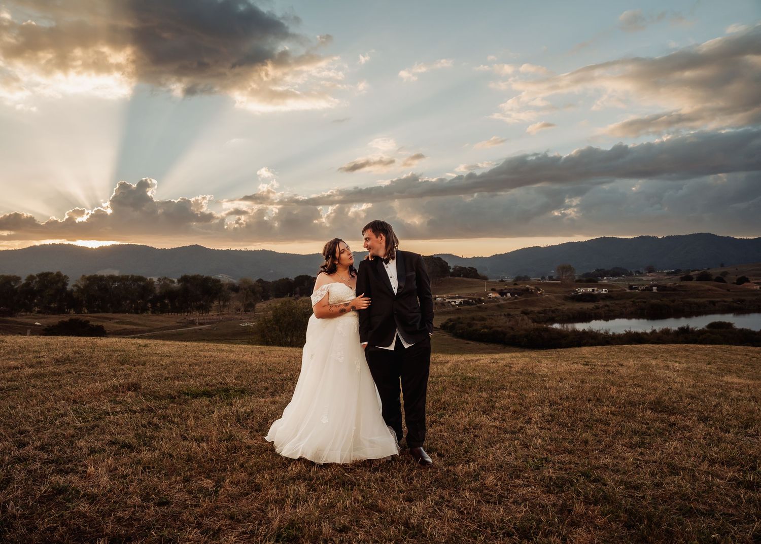 Bride and groom sharing a tender moment in a golden field at sunset with mountain views.